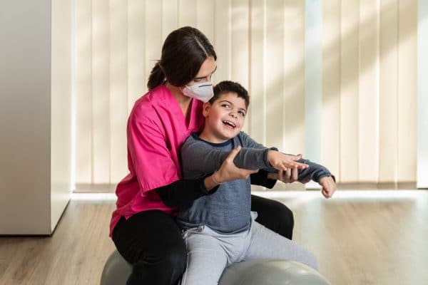 Disabled Child And Physiotherapist On Top Of A Peanut Gym Ball Doing Balance Exercises