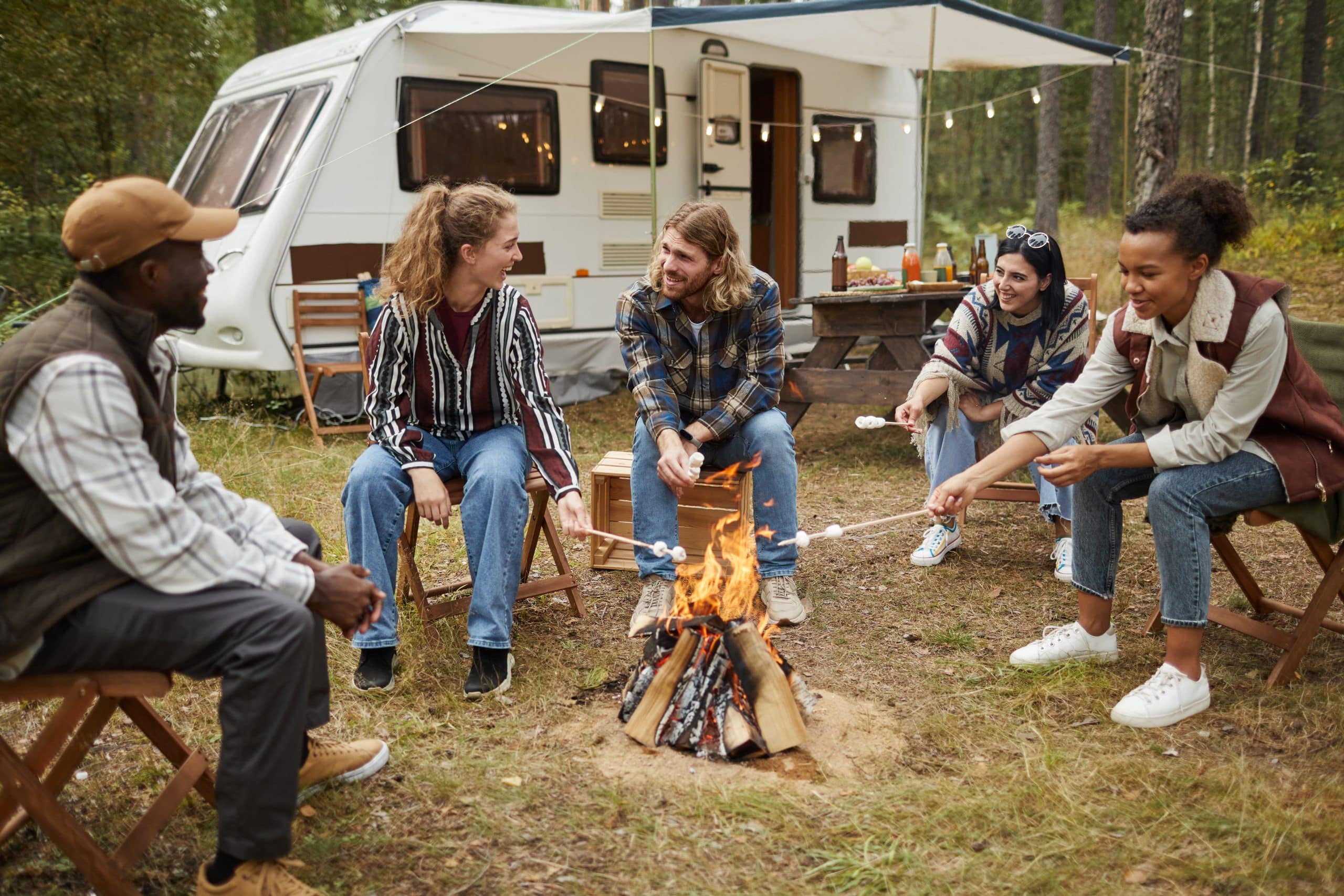 Diverse group of young people roasting marshmallows while enjoying camping with friends in forest, copy space